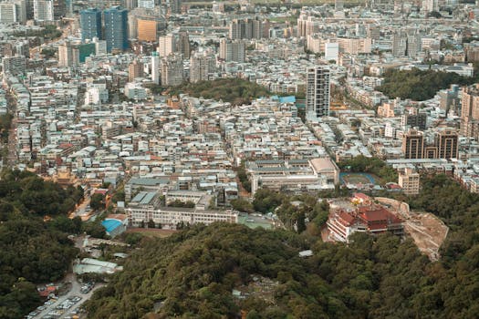 Expansive aerial view of a dense urban cityscape surrounded by lush greenery, showcasing urban and natural blend.